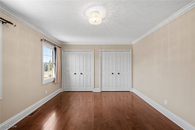 unfurnished bedroom with visible vents, two closets, baseboards, hardwood / wood-style floors, and a textured ceiling