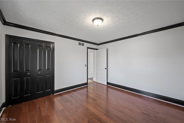 unfurnished bedroom featuring visible vents, dark wood finished floors, a closet, crown molding, and baseboards