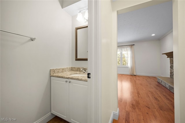 bathroom with ornamental molding, wood finished floors, a fireplace, baseboards, and vanity