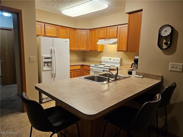 kitchen with under cabinet range hood, a breakfast bar, a peninsula, white appliances, and a textured ceiling