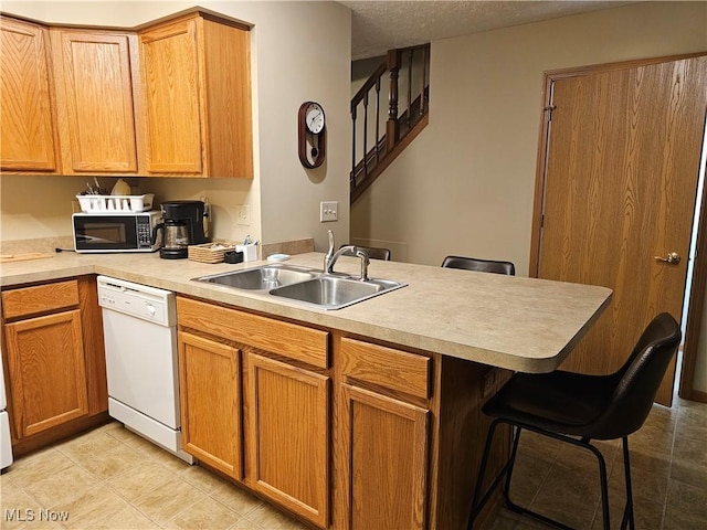 kitchen featuring black microwave, dishwasher, a kitchen breakfast bar, a peninsula, and a sink