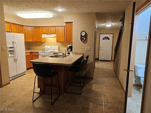 kitchen with under cabinet range hood, a kitchen breakfast bar, a peninsula, white appliances, and a sink