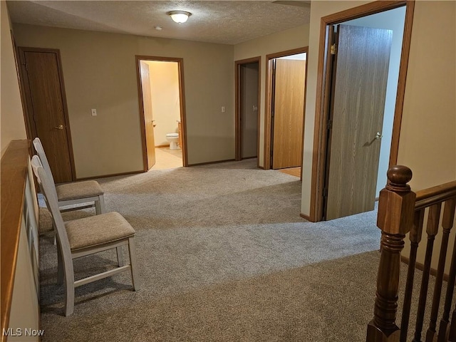 corridor featuring light colored carpet, a textured ceiling, and baseboards