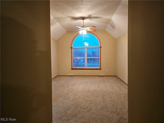 carpeted empty room featuring baseboards, a textured ceiling, a ceiling fan, and vaulted ceiling