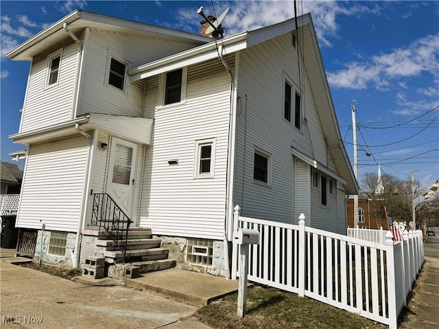 back of house with entry steps, a chimney, and fence