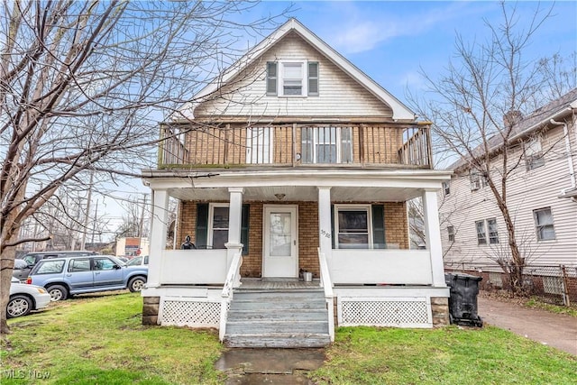 view of front of property featuring a front lawn, a balcony, covered porch, and brick siding