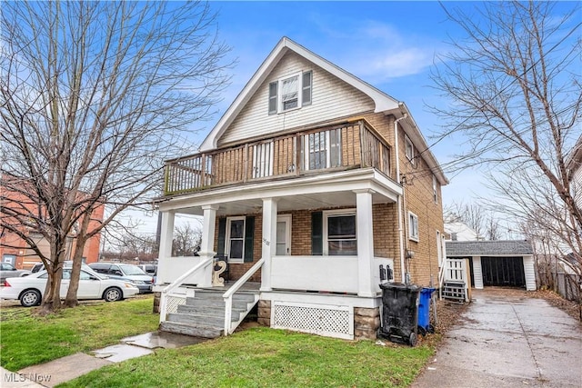 view of front of property featuring a balcony, a porch, an outdoor structure, a front lawn, and brick siding