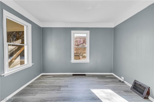 spare room featuring wood finished floors, visible vents, and baseboards