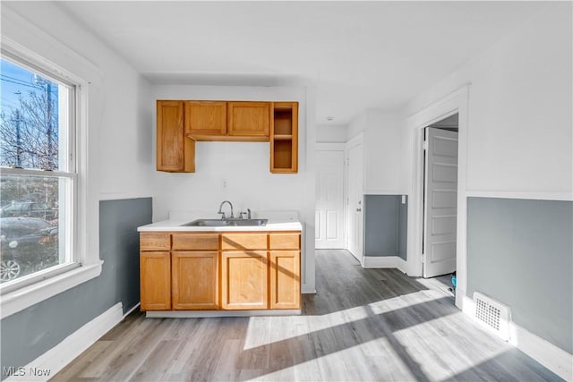 kitchen with light wood finished floors, visible vents, baseboards, light countertops, and a sink