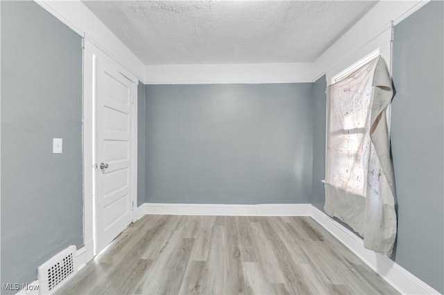 spare room featuring baseboards, wood finished floors, visible vents, and a textured ceiling