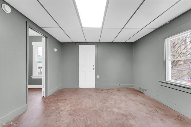 spare room featuring wood finished floors, plenty of natural light, a paneled ceiling, and baseboards