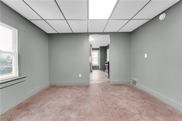 spare room featuring wood finished floors, visible vents, a drop ceiling, and baseboards