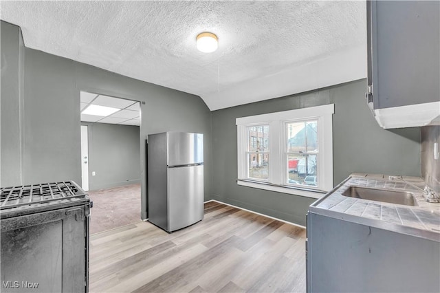 kitchen featuring light wood-type flooring, tile counters, gas range oven, and freestanding refrigerator