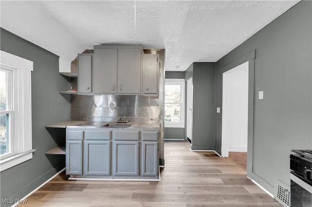 kitchen featuring open shelves, light wood finished floors, gray cabinetry, and a sink