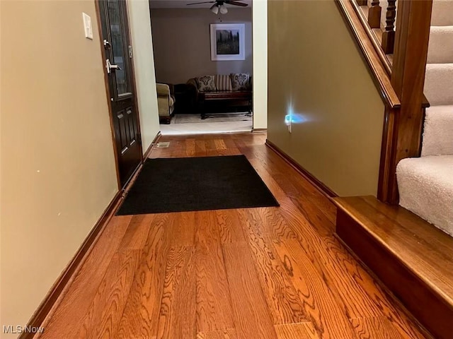 hallway featuring baseboards, wood finished floors, and stairs