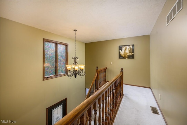 hall featuring carpet, an inviting chandelier, an upstairs landing, and visible vents