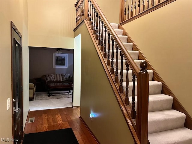 stairway featuring visible vents, a high ceiling, and wood finished floors