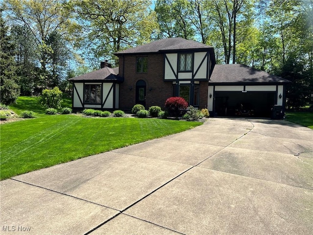 english style home featuring driveway, a chimney, a front lawn, a garage, and brick siding