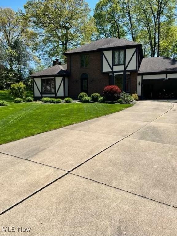 view of side of home with an attached garage, a chimney, driveway, and a yard