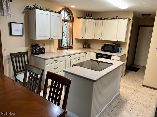 kitchen with a sink, black appliances, light countertops, white cabinetry, and a center island