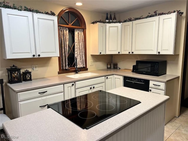 kitchen with a sink, black appliances, light countertops, and white cabinetry