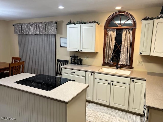 kitchen with a sink, stovetop, light countertops, and white cabinetry