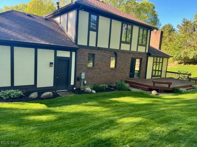 back of property featuring stucco siding, a lawn, a wooden deck, brick siding, and a chimney