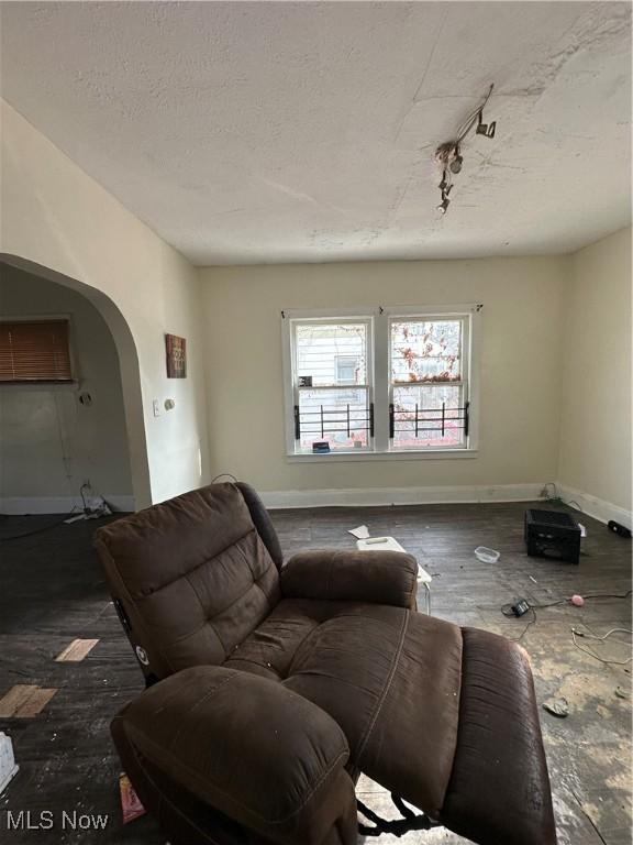 living area featuring baseboards, a textured ceiling, and arched walkways