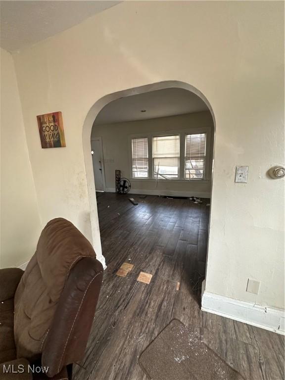 corridor featuring wood finished floors, arched walkways, and baseboards