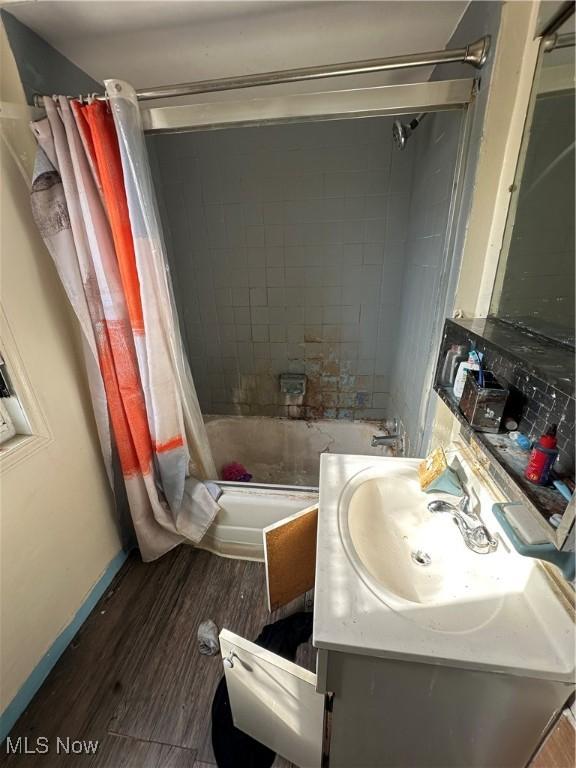 full bath featuring baseboards, vanity, wood finished floors, and shower / bath combo