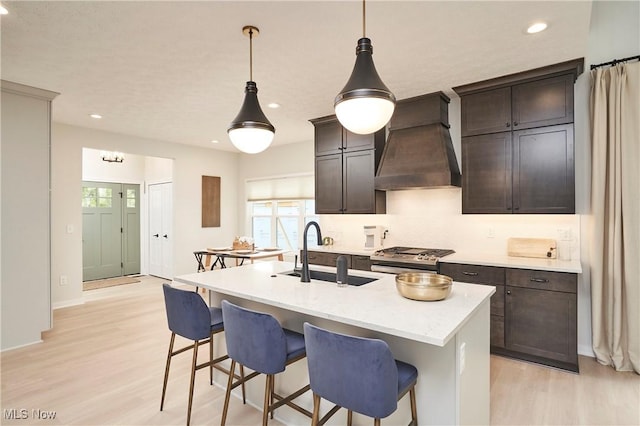 kitchen featuring gas range, premium range hood, light wood finished floors, and a sink