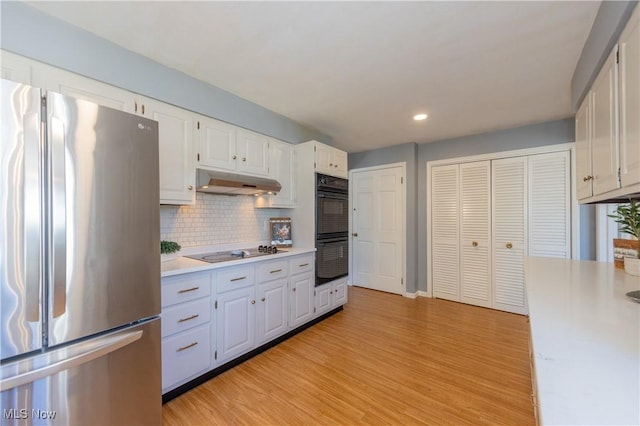 kitchen featuring tasteful backsplash, under cabinet range hood, light wood-type flooring, light countertops, and black appliances