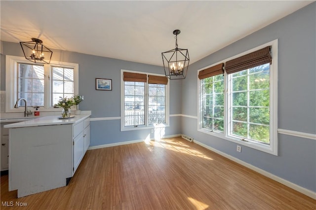 unfurnished dining area featuring a sink, light wood-type flooring, a notable chandelier, and a healthy amount of sunlight