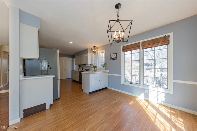 kitchen with light wood finished floors, baseboards, light countertops, freestanding refrigerator, and a notable chandelier