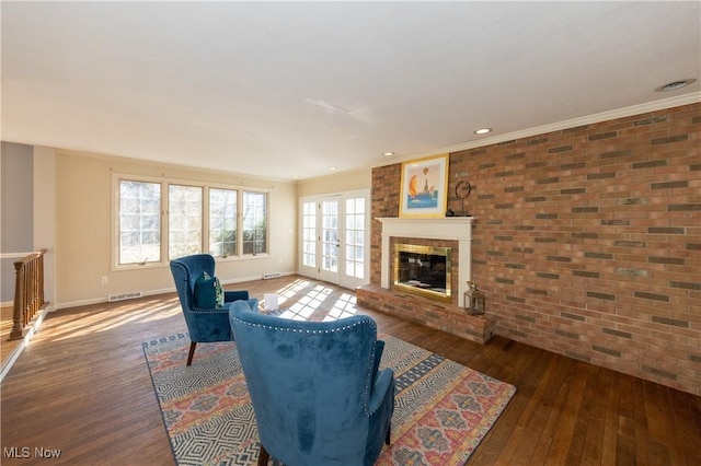 living area with a brick fireplace, wood finished floors, visible vents, and brick wall