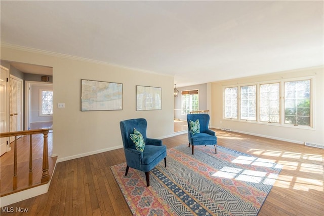 living area with visible vents, baseboards, crown molding, and hardwood / wood-style flooring