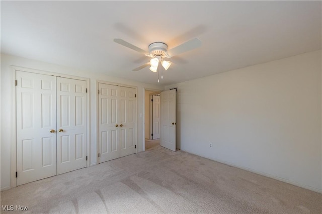 unfurnished bedroom with two closets, carpet, and a ceiling fan