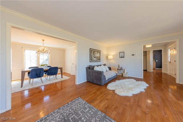 living room with an inviting chandelier, crown molding, wood finished floors, and baseboards