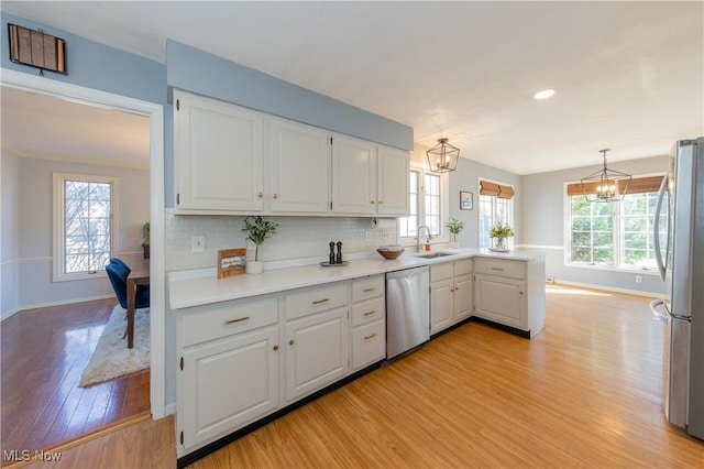 kitchen with a chandelier, a peninsula, white cabinets, stainless steel appliances, and a sink