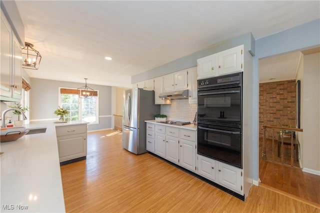 kitchen featuring dobule oven black, under cabinet range hood, a sink, freestanding refrigerator, and an inviting chandelier