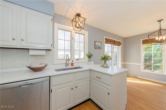 kitchen with a sink, stainless steel dishwasher, white cabinetry, an inviting chandelier, and a peninsula