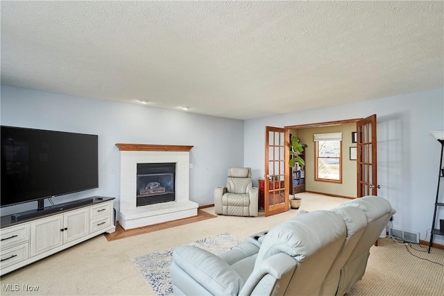 living area featuring visible vents, light colored carpet, french doors, and a glass covered fireplace