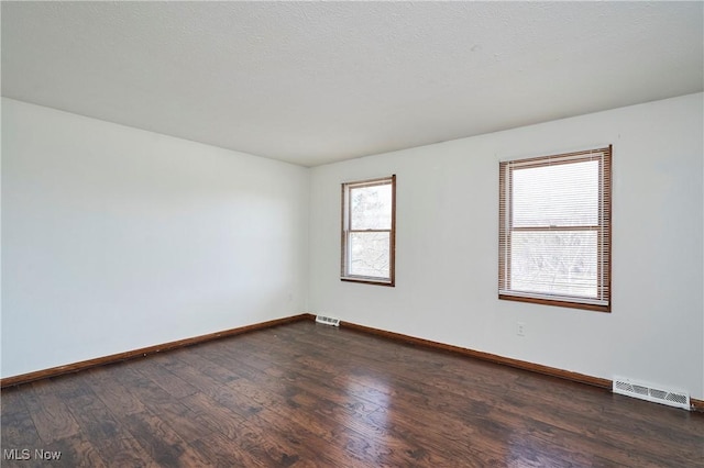 empty room featuring dark wood finished floors, baseboards, visible vents, and a textured ceiling