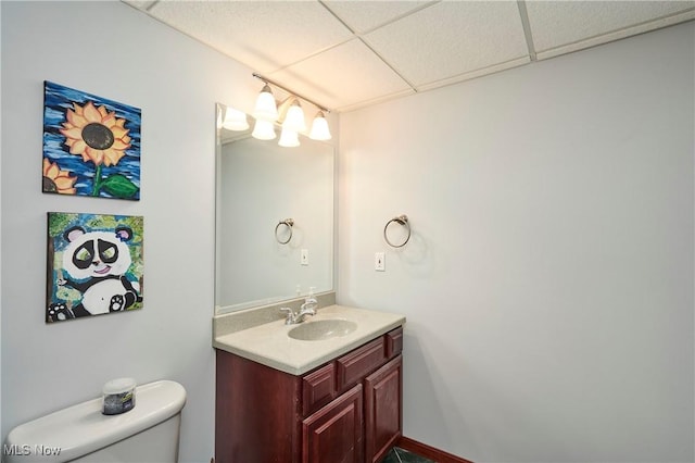 half bath with a drop ceiling, toilet, and vanity