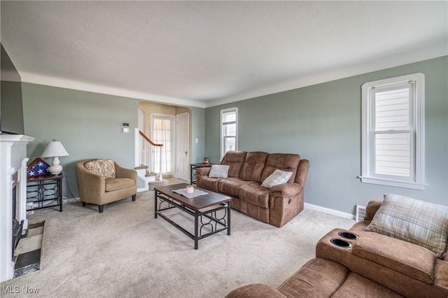 living room with baseboards, stairway, a fireplace with flush hearth, carpet flooring, and a textured ceiling