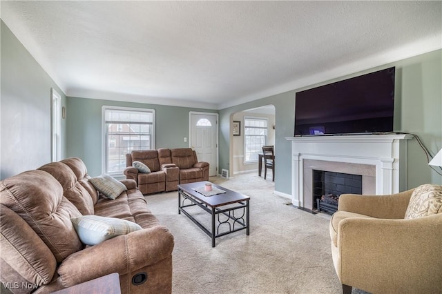 living area with light carpet, a fireplace with flush hearth, a textured ceiling, and baseboards