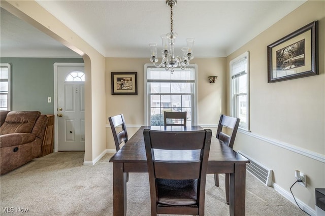 dining space with baseboards, ornamental molding, light carpet, an inviting chandelier, and arched walkways