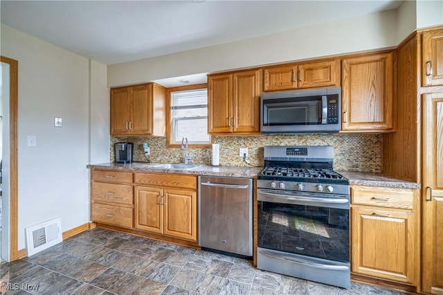 kitchen featuring brown cabinetry, visible vents, a sink, decorative backsplash, and appliances with stainless steel finishes