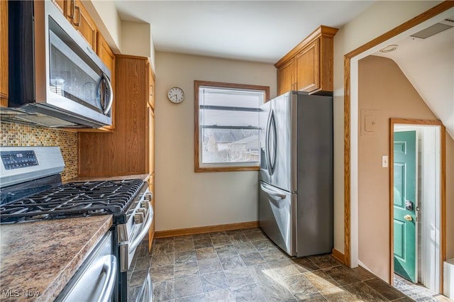 kitchen featuring tasteful backsplash, baseboards, appliances with stainless steel finishes, brown cabinetry, and stone finish floor