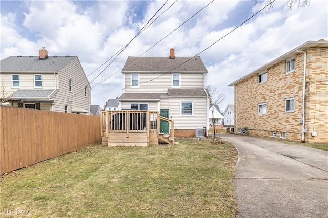 back of property with fence, a wooden deck, a lawn, cooling unit, and a chimney